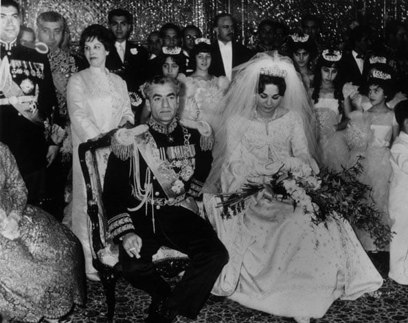 The Shah of Persia,  wears the blue uniform of Commander-in-Chief as he sits beside his bride Farah Diba wearing a Dior dress of silk gaberdine embroidered with rhinestones and silver.